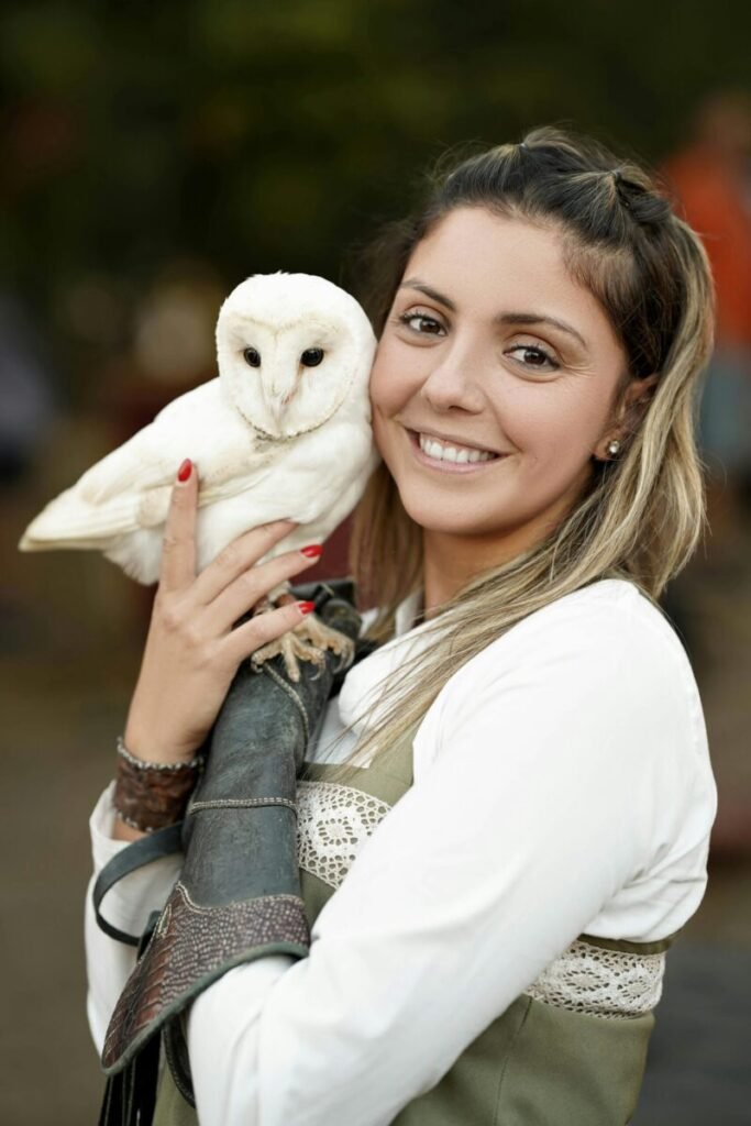 Smiling woman holding a barn owl outdoors, showcasing a bond with wildlife.