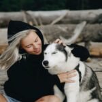 A woman in a hoodie petting her Siberian husky outdoors.