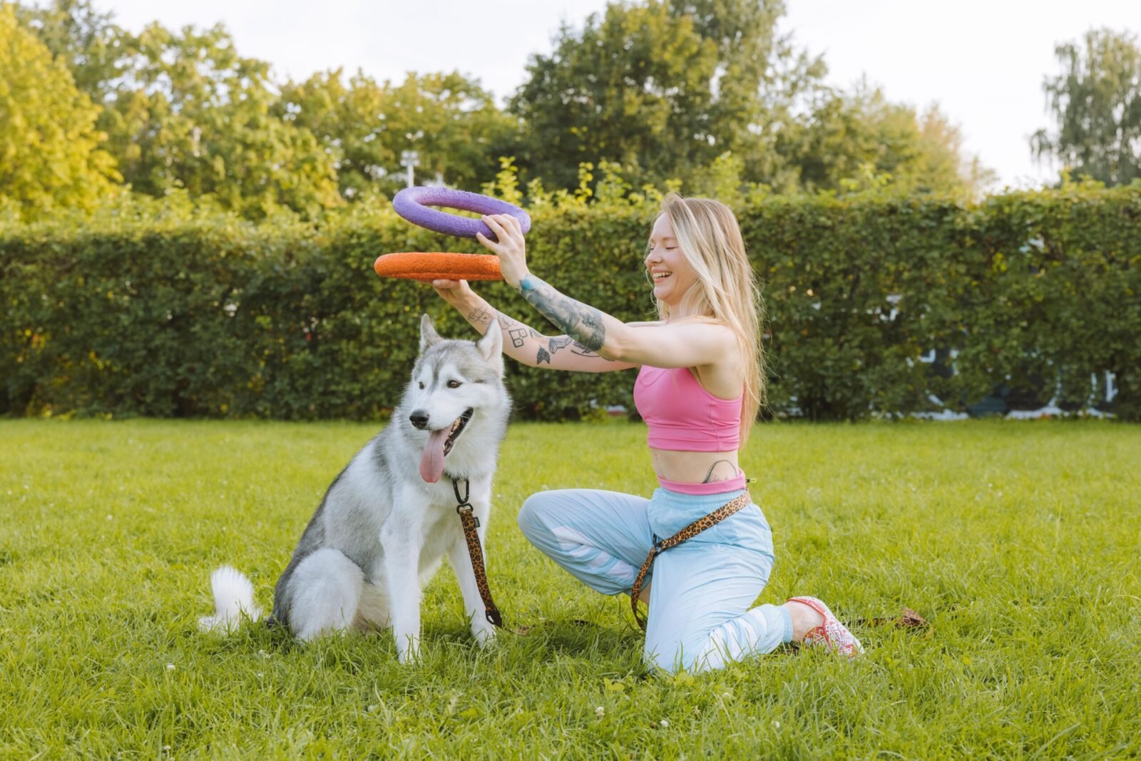 Woman enjoying a playful moment with her husky dog outdoors in a sunny park setting.
